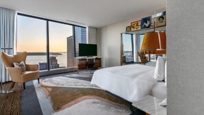 Une chambre d’hôtel moderne dotée d’un grand lit, d’un bureau avec un téléviseur à écran plat, d’une chaise et offrant une vue sur le panorama de la ville.