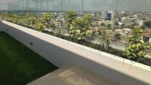 Une terrasse sur le toit dotée d’une balustrade en verre, d’une pelouse verdoyante et offrant une vue sur le paysage urbain.