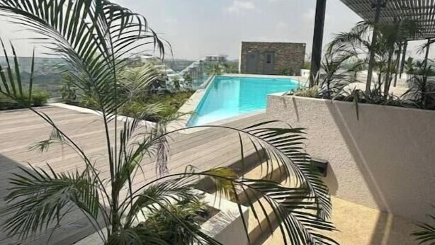 Un espace piscine offrant une vue sur une chaîne de montagnes, entouré de palmiers et doté d’un patio couvert.