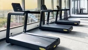 Une salle de sport où les tapis de course sont alignés contre un mur, face à de grandes fenêtres qui donnent sur la ville.