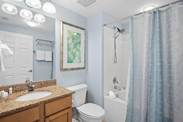 A bathroom with a granite countertop sink, a white toilet, a shower with a glass door, and a framed abstract painting on the wall. - Palms Resort #1603 Jr. 2BR (Destin)