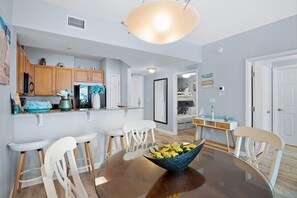 A modern kitchen with wooden cabinets, a dining table with chairs, and a large bowl of fruit. - Palms Resort #1603 Jr. 2BR (Destin)