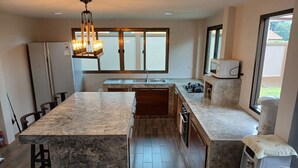 A modern kitchen with a marble island, a built-in oven, and a large window providing natural light. - Peaceful Resort-Style pool villa in Doi Saket, Chiang Mai (Tambon Choeng Doi)