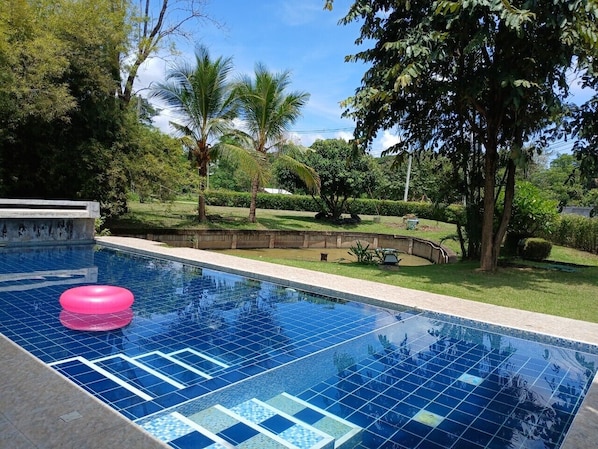 A swimming pool with a pink float, surrounded by lush greenery and palm trees. - Peaceful Resort-Style pool villa in Doi Saket, Chiang Mai (Tambon Choeng Doi)