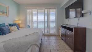 A bedroom with a bed, a dresser, a ceiling fan, a TV, and a window with blinds. - Ocean Reef 1105 (Panama City Beach)