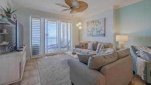 A living room with a sofa, a TV, and a ceiling fan. There is a sliding glass door leading to a balcony. - Ocean Reef 1105 (Panama City Beach)