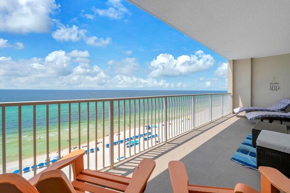 A balcony with a view of the beach and ocean, wooden chairs, a small table, and a hanging light fixture.