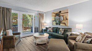 A living room with a sofa, armchairs, a coffee table, and a painting on the wall. - Sea Oats 111 (Fort Walton Beach)