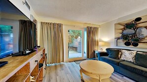 A living room with a TV, wooden furniture, a sofa, and a painting on the wall. - Sea Oats 111 (Fort Walton Beach)