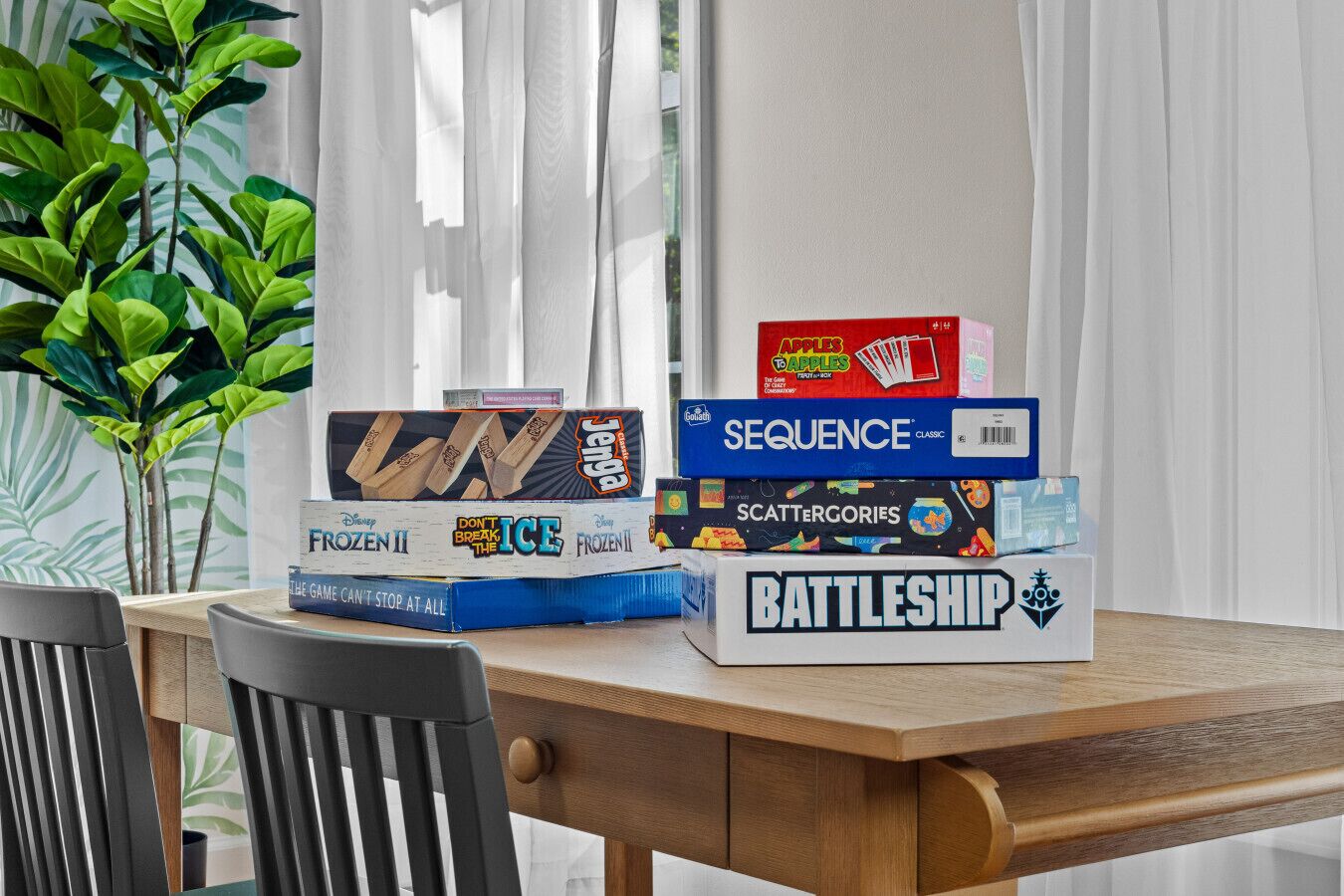 Puinen pöytä, jonka päällä on pino lautapelejä, kuten Frozen II, Sequence, Scattergories ja Battleship.