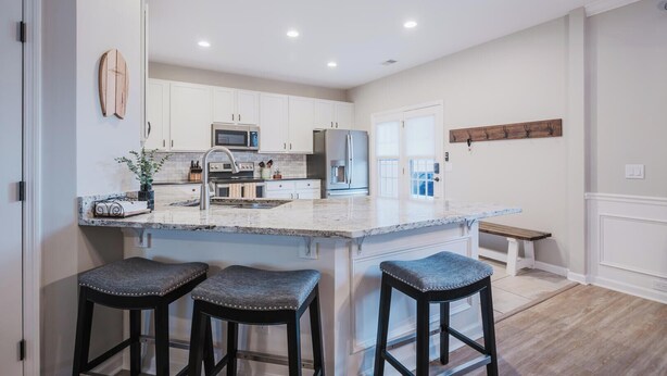 Una cocina moderna con armarios blancos, una isla grande con taburetes de bar, electrodomésticos de acero inoxidable y un banco de madera.