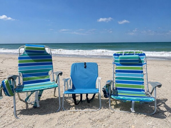 Két csíkos strandnapágy egy homokos strandon, ahonnan az óceánra nyílik kilátás.