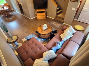Ein modernes Wohnzimmer mit einem braunen Ecksofa, einem runden Couchtisch und einem Flachbildfernseher auf einem Holzständer.