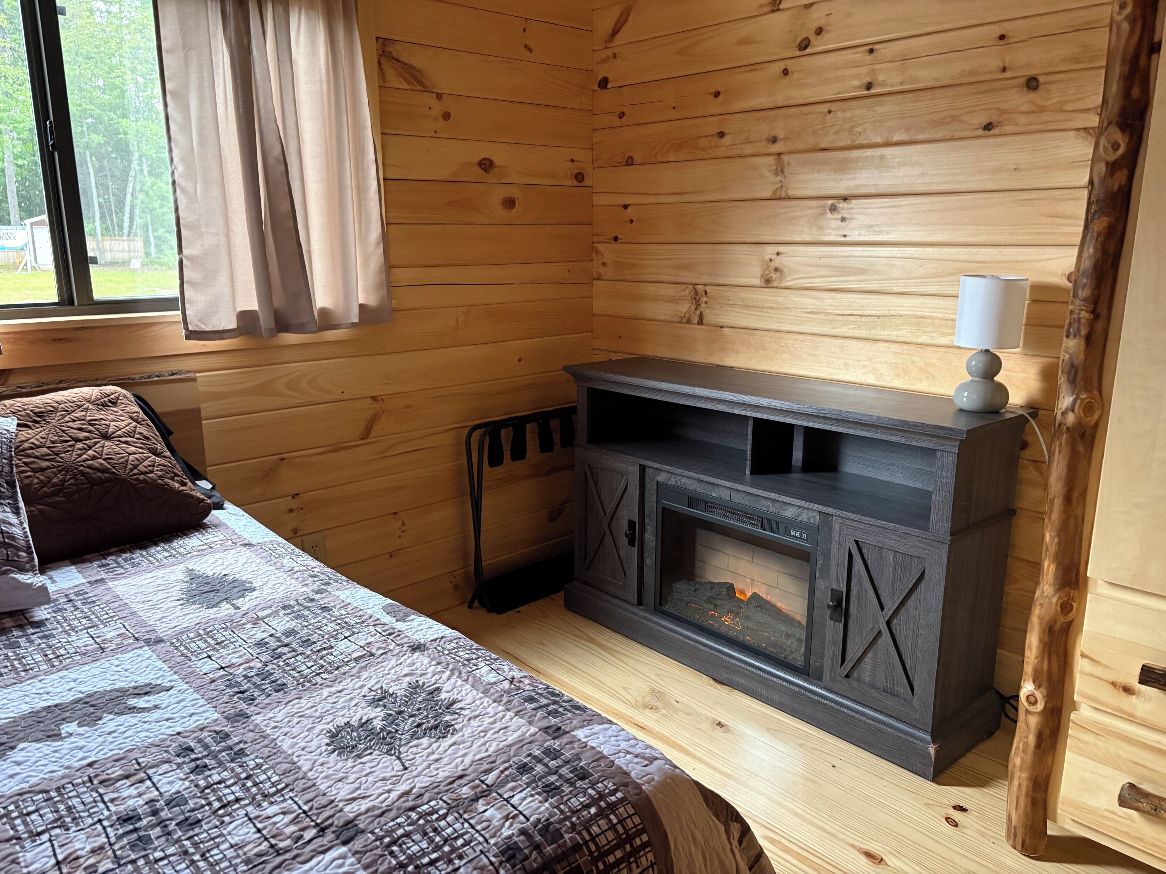 A wooden cabin room with a bed, a fireplace, and a window with curtains.