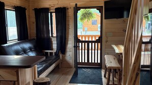 Ein Holzblockhaus-Interieur mit einer schwarzen Ledersofa, einem Esstisch und einem Deckenventilator.