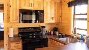 Ein Interieur einer Holzhütte mit einer Küche, die eine Mikrowelle, einen Herd und ein Spülbecken umfasst.