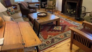 A cozy living room with a fireplace, wooden furniture, and a large rug. - Warren Village home steps from bubbling brook (Warren)
