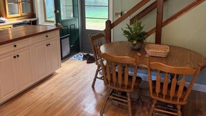Une cuisine avec des meubles de rangement en bois, une table à manger avec des chaises, un escalier en bois et une porte donnant sur l’extérieur.