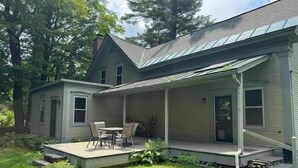 Une maison à deux étages avec un porche couvert, une petite terrasse et un jardin devant.