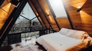 A cozy attic bedroom with a sloped ceiling, a bed with white bedding, and a stone wall in the background. - Chalet Goliat by Woodland Cabins (Ciudad López Mateos)
