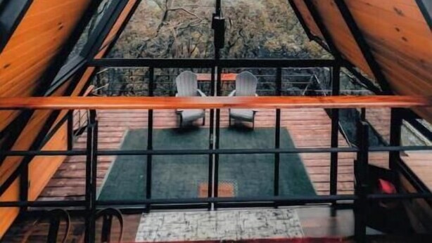A triangular wooden cabin with a central skylight, a small seating area with chairs, and a view of trees outside. - Chalet Goliat by Woodland Cabins (Ciudad López Mateos)