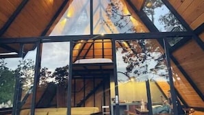 A modern, triangular-roofed structure with a glass facade, wooden interior, and a sofa area. - Chalet Goliat by Woodland Cabins (Ciudad López Mateos)