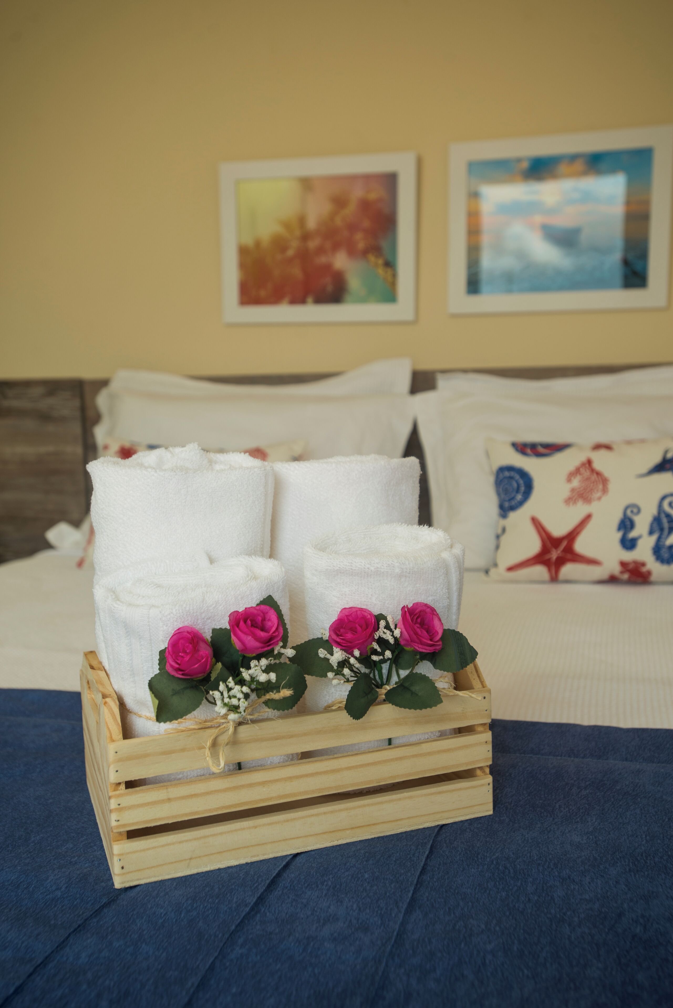A neatly made bed with white towels and a wooden crate with pink roses.