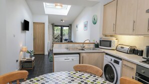 Une cuisine compacte équipée d’un lave-linge, d’un four à micro-ondes et d’un grille-pain. Elle comprend également un coin repas avec une table et des chaises à motifs à pois.