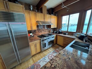Une cuisine moderne avec des meubles en bois, des appareils en acier inoxydable, un plan de travail en granit et une vue sur l’eau.