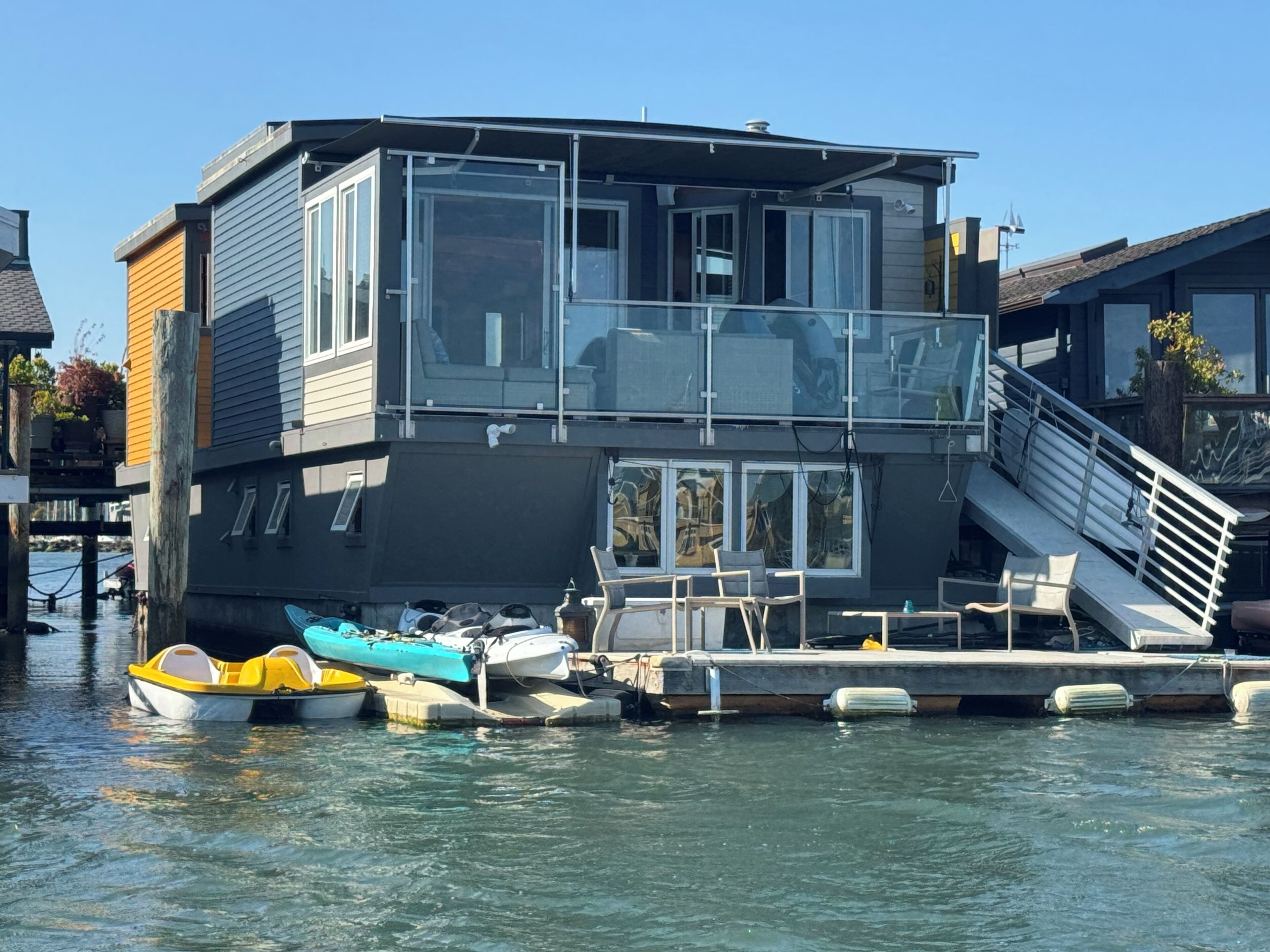 Ein modernes Hausboot mit Glasbalkon, liegt an einer Anlegestelle mit mehreren Booten.
