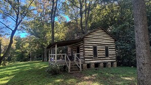 A rustic log cabin with a porch and a small deck, surrounded by trees and grass. - Back in Time! River Log Cabin-Off Grid (Concord)