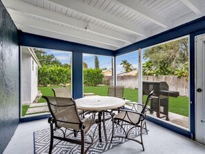 A covered patio with a round table and chairs, large windows, and a view of a backyard. - 1.5 miles 5 min 🚗 to beaches, King Beds, BBQ, Nintendo Switch 🎮, Pet friendly 🐶. (Naples)