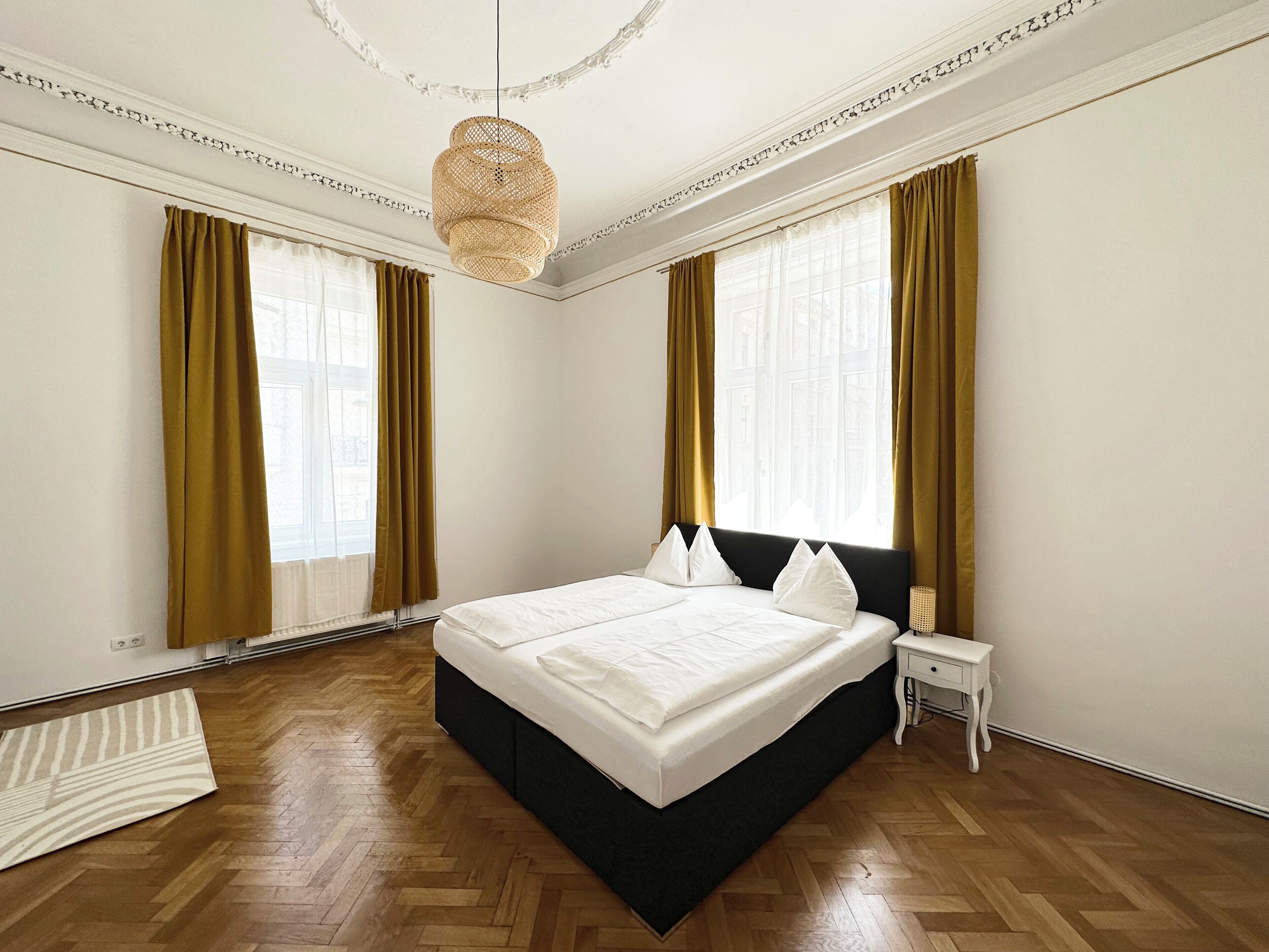 A large bed with a black headboard, two white pillows, and a bedside table with a lamp.