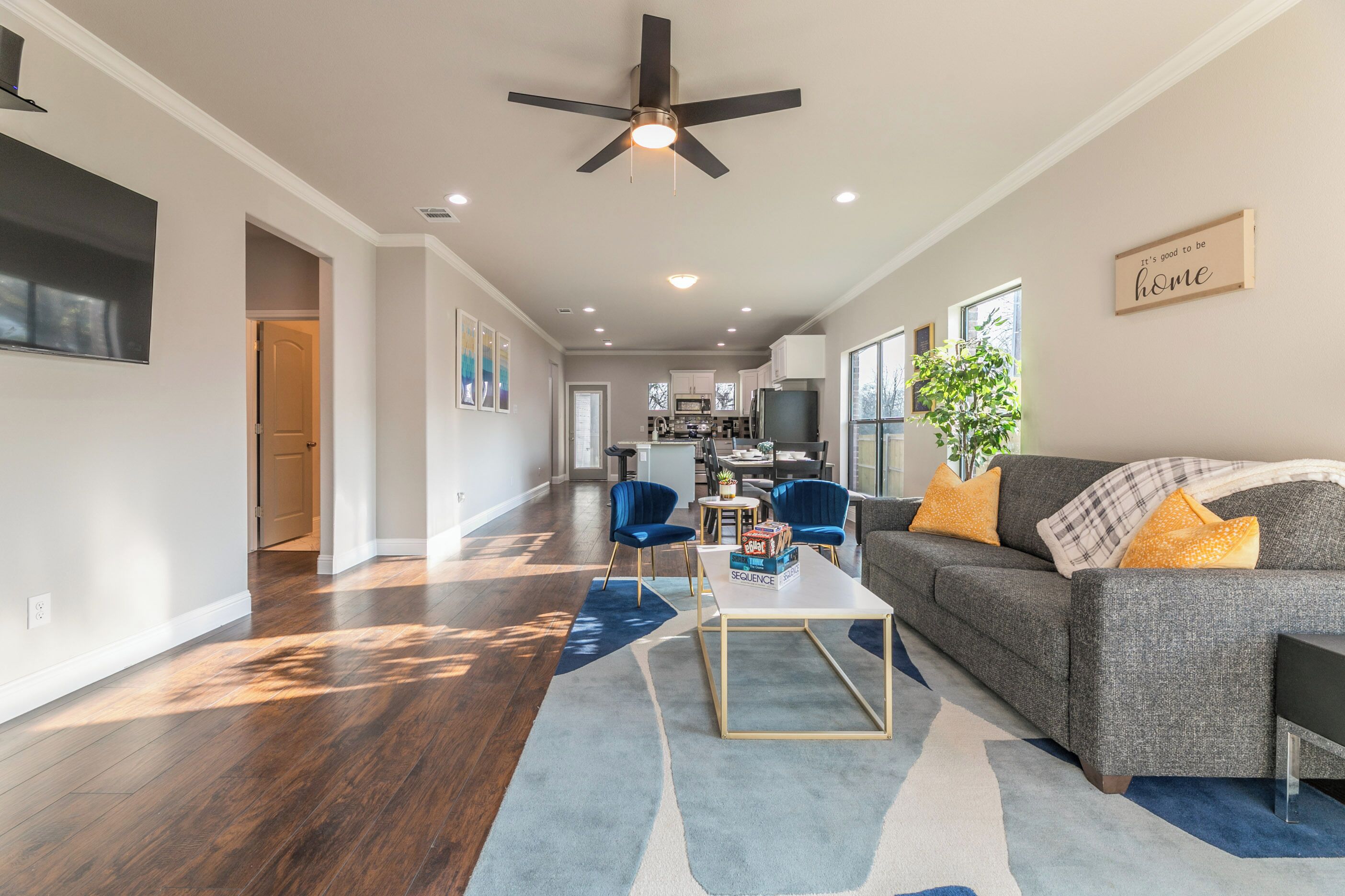 A spacious living area with a grey sofa, blue chairs, a coffee table, and a ceiling fan.