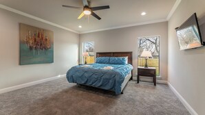 Une chambre à coucher avec un lit, un ventilateur de plafond, une fenêtre et un tableau accroché au mur.