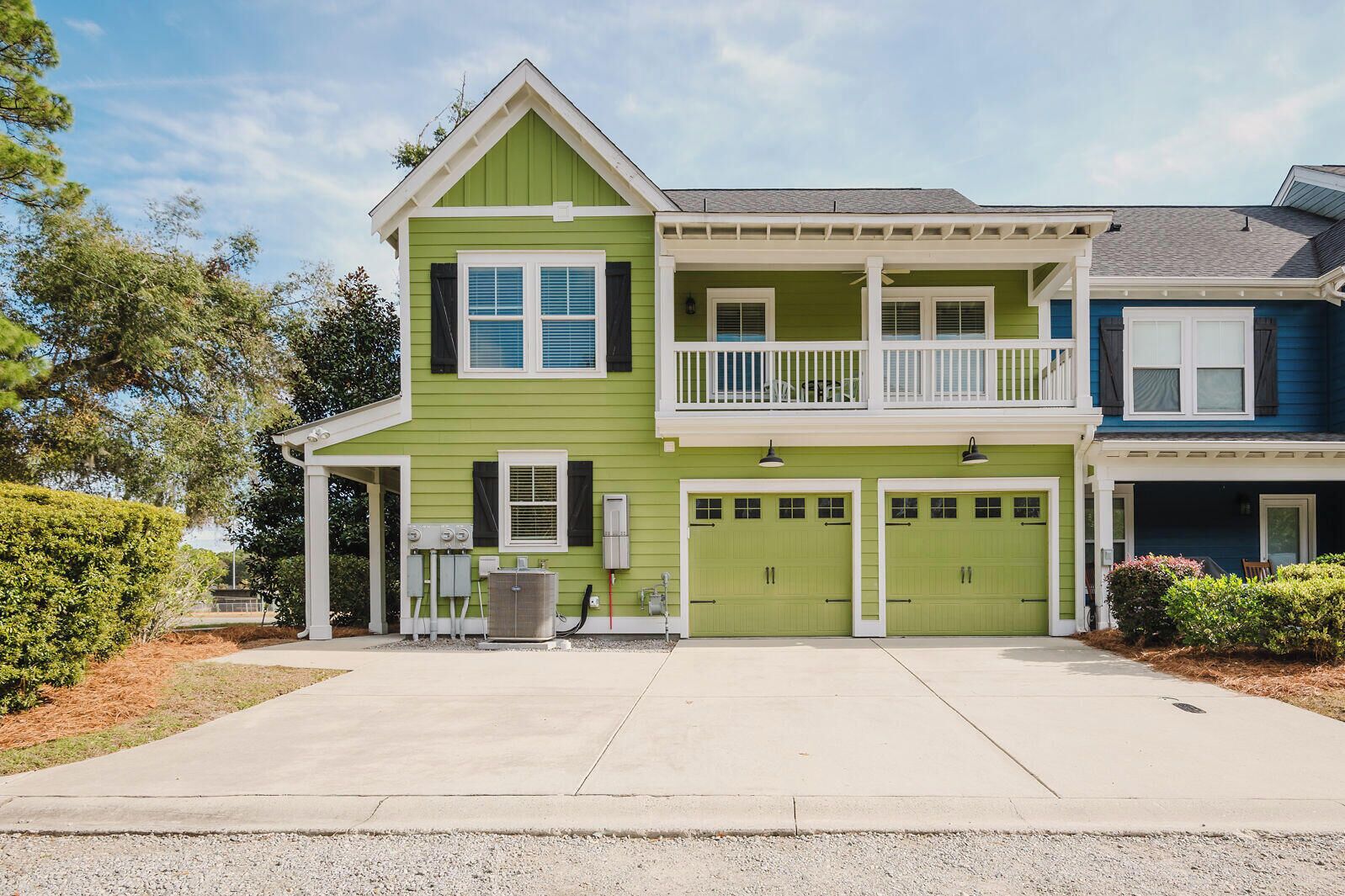 Une maison à deux étages avec une façade verte, un balcon au deuxième étage et deux portes de garage.