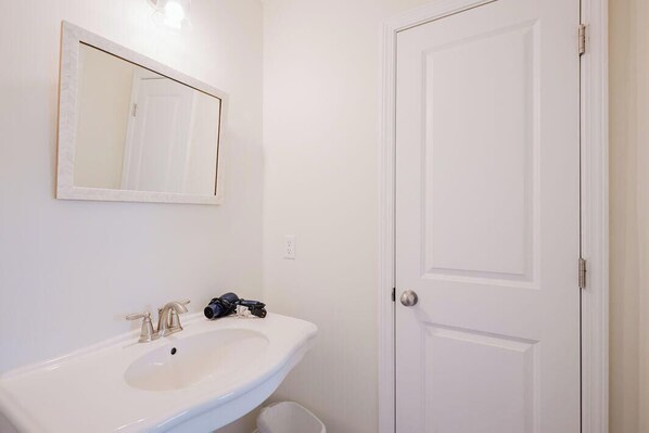 Un baño con un lavamanos blanco, un espejo y una puerta cerrada.