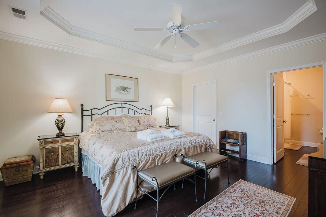 Une chambre à coucher comprenant un lit, des tables de chevet, un banc, un ventilateur de plafond et une porte donnant sur une autre pièce.