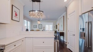 Une cuisine moderne avec des meubles blancs, un réfrigérateur en acier inoxydable et un lustre.