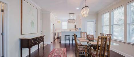 A spacious dining area with a long wooden table and chairs, a chandelier, and a red patterned rug.