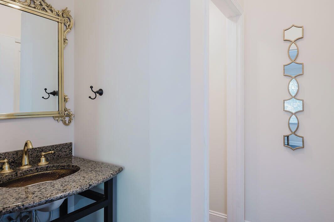 Un baño con lavamanos de encimera de granito, detalles dorados y un espejo grande y decorativo.
