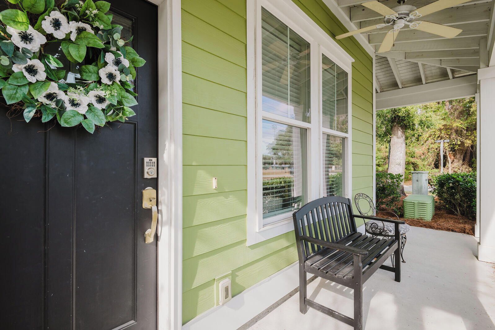 A house with a dark front door, a green exterior, and a porch with a bench.