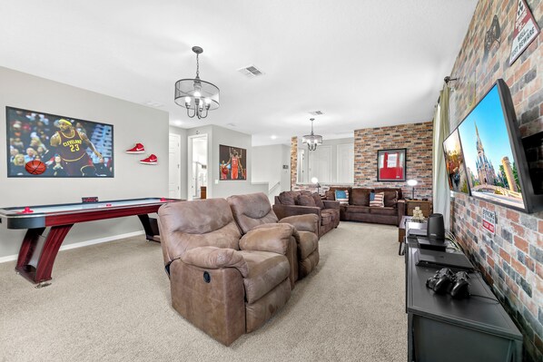 A living room with a pool table, reclining sofas, and a television. - 5BR Pool Home, Near Disney, Orlando (Kissimmee)