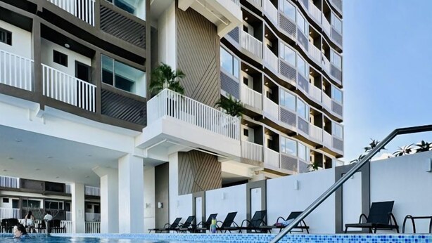 Et moderne hotel med flere balkoner, en swimmingpool og liggestole.