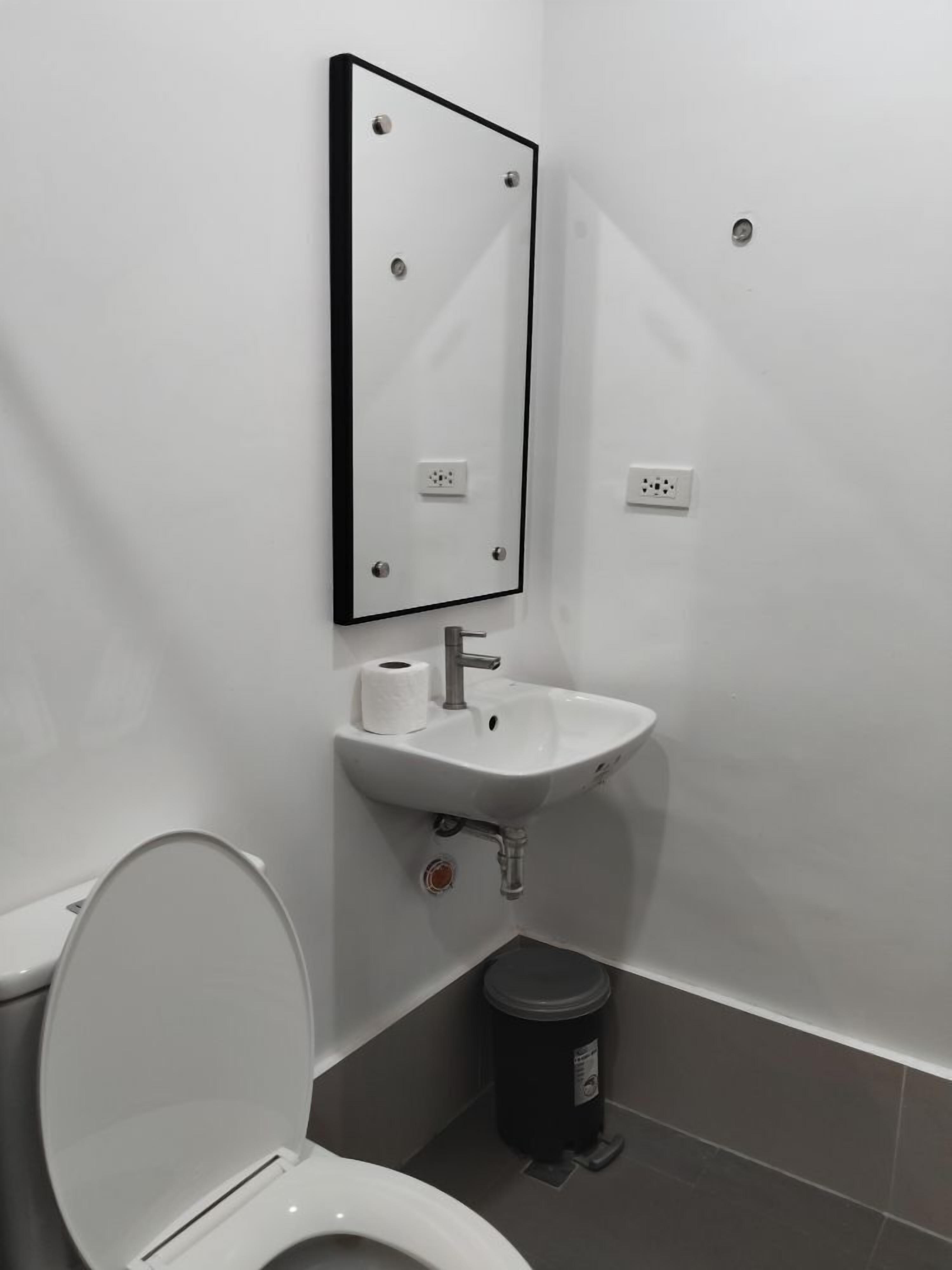 A small, modern bathroom with a white toilet, a sink with a mirror above it, and a trash bin.