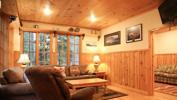A cozy living room with wooden walls and floors, a brown leather sofa, a wooden coffee table, and two lamps.