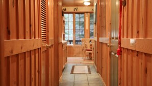 A wooden hallway with a tiled floor leading to a room with a window and a chair.
