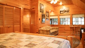A cozy log cabin room with a large bed, a wooden ceiling, and a fireplace.