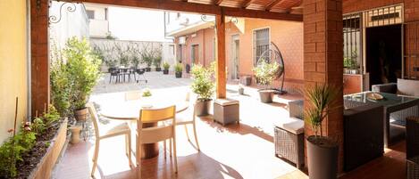 An outdoor patio with a round table and chairs, surrounded by potted plants and wicker furniture.