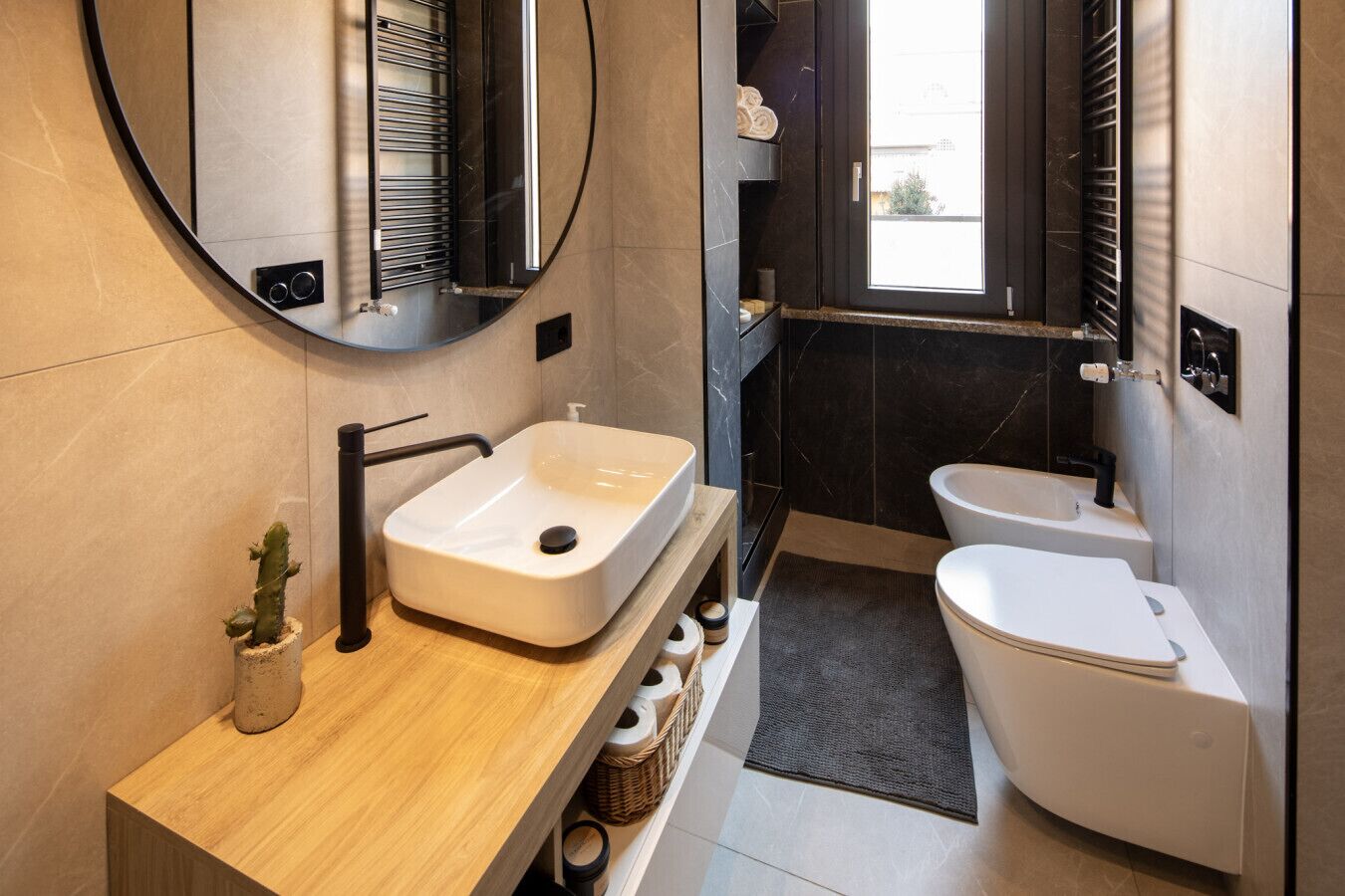 Een moderne badkamer met een houten wastafelmeubel, een witte wastafel, een ronde spiegel, een toilet en een douchehoek.